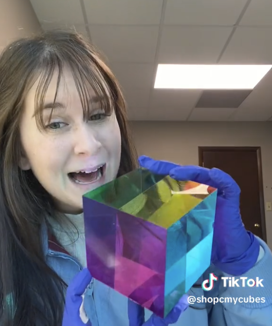 CMYCUBES Woman in blue gloves smiles while holding a colorful, transparent cube in an indoor setting.