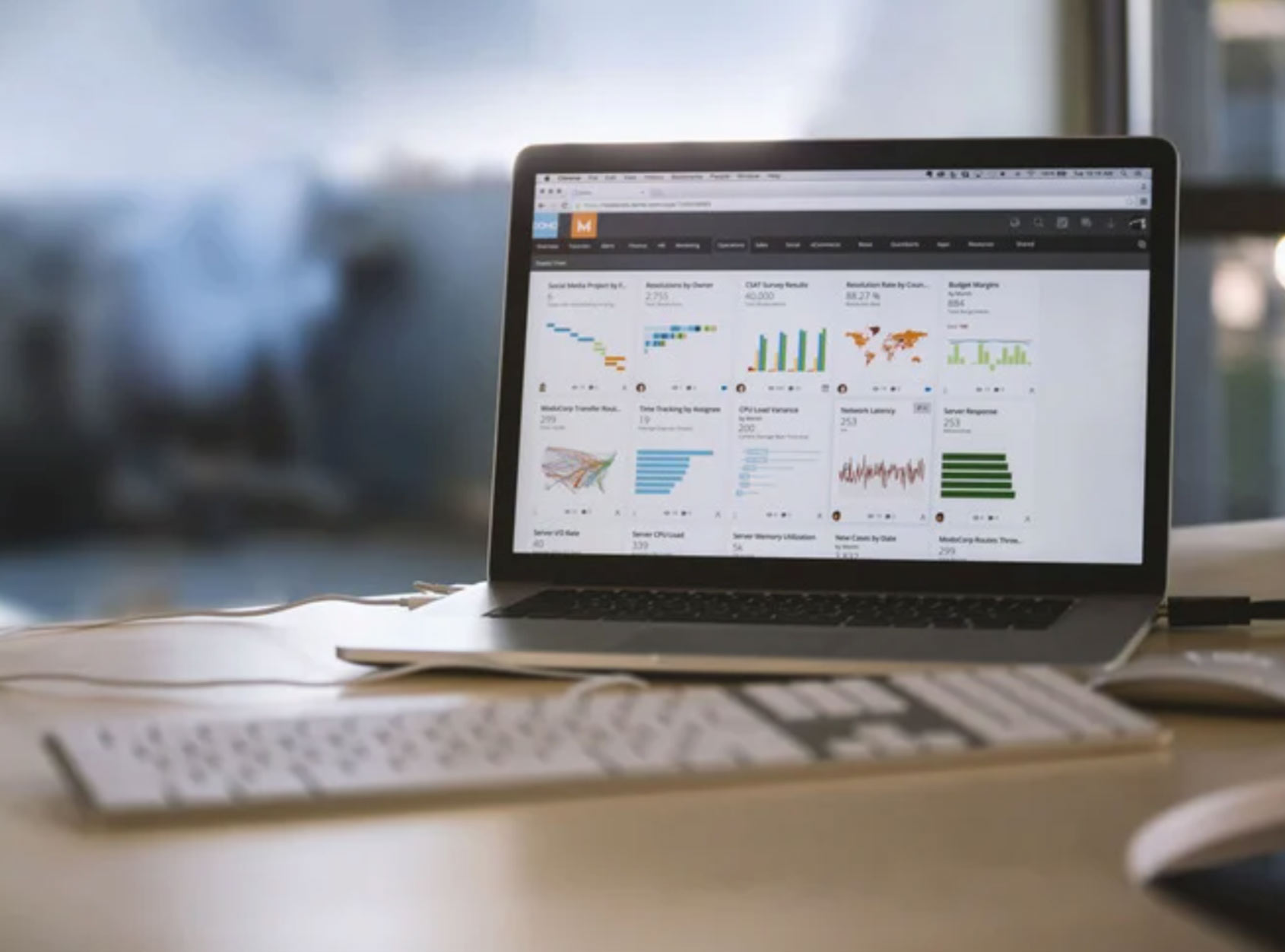 Laptop on a desk displaying various charts and graphs on its screen, with a keyboard in front.