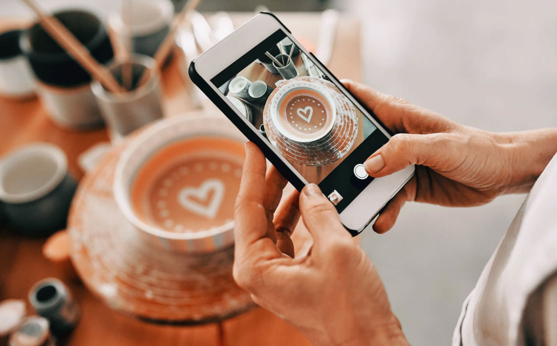 smkt-img Person taking a photo of a heart-decorated ceramic bowl with a smartphone in a pottery studio.